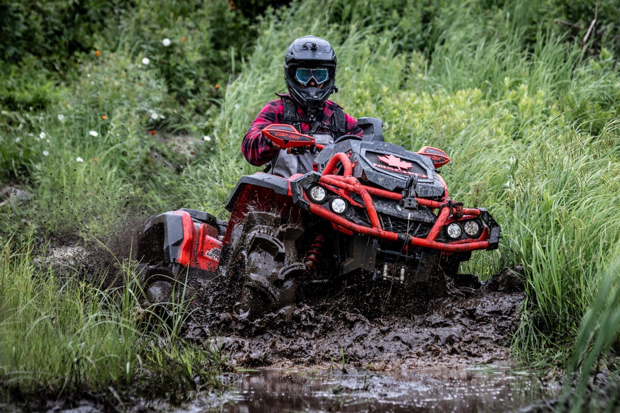 Un quad, avec les roues arrières enfoncées dans la boue, avance dans un sentier marécageux.
