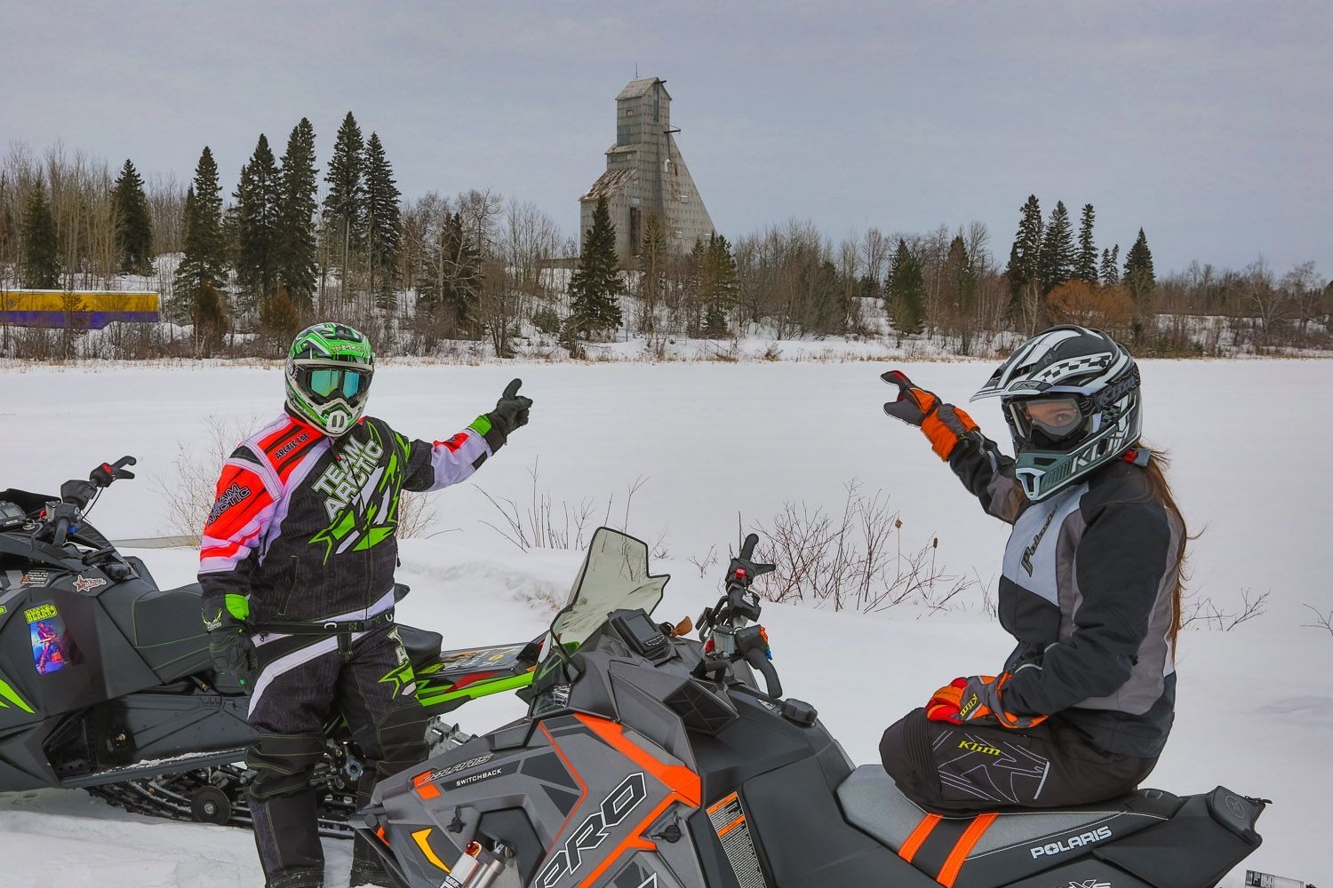 Deux motoneigiste pointent vers un chevalement de mine, au loin, à Timmins.