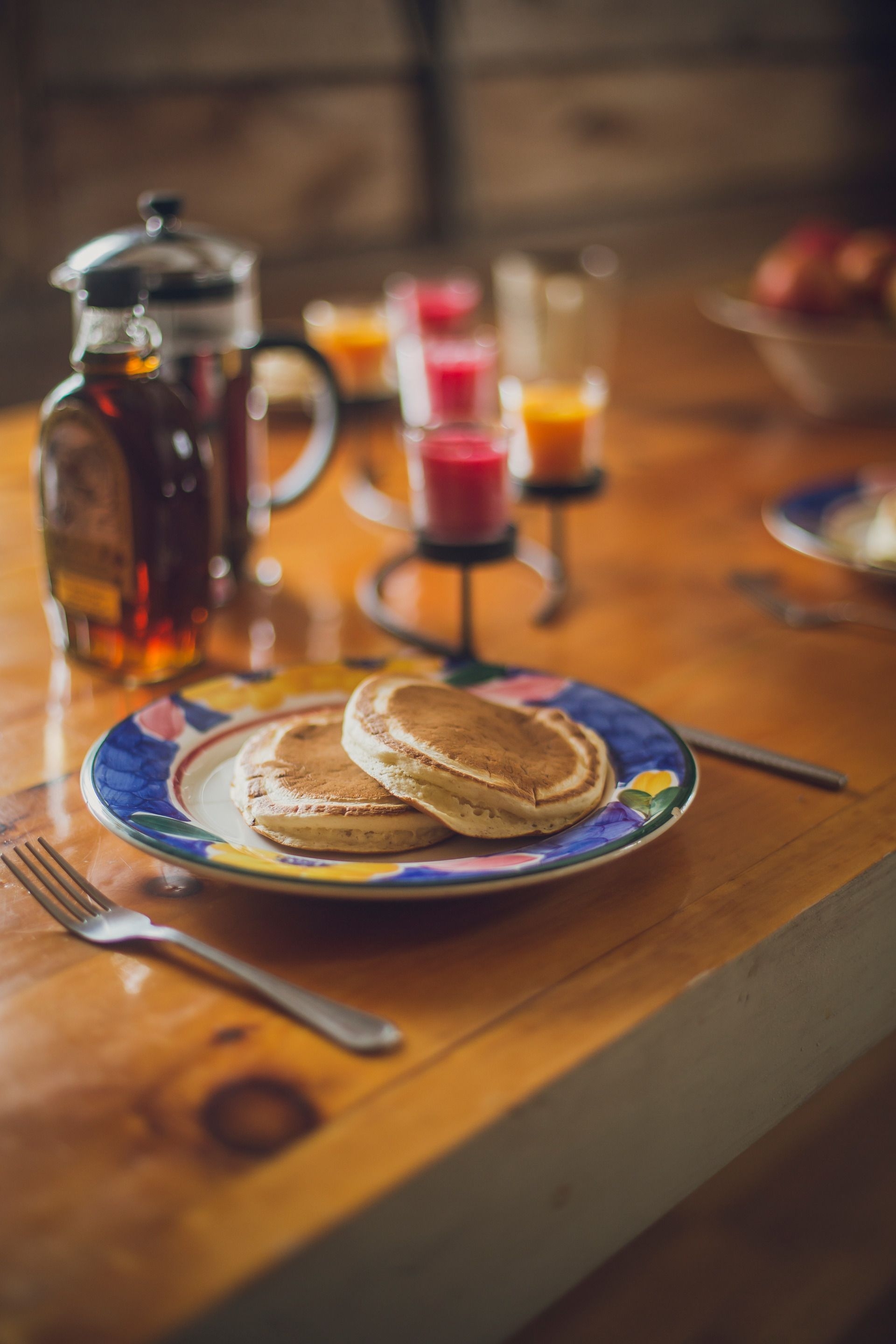 Dans une assiette, sur une table de bois, deux crêpes. À côté, un pot de sirop d'érable en vitre. 