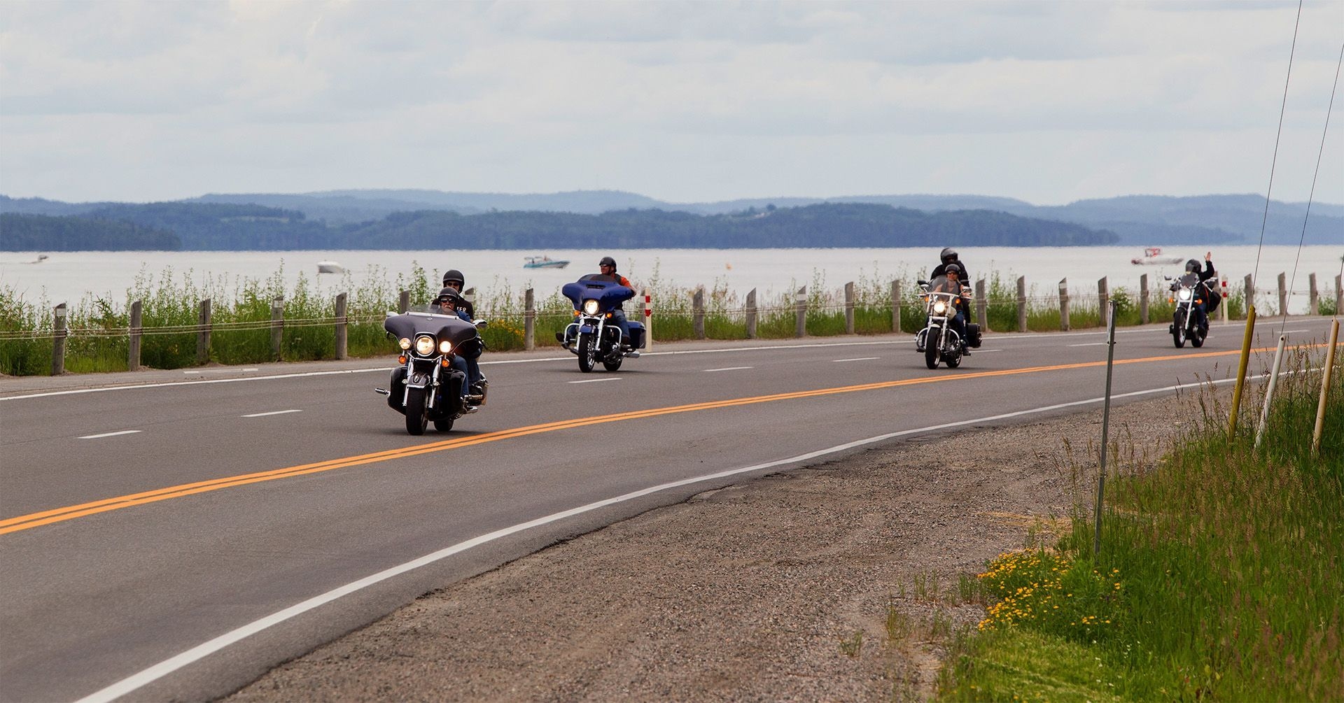 Trois motocyclettes circulent sur la route, sur le bord de l'eau.