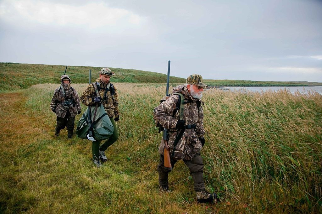 Three people walking through a field preparing on their way to a hunt.