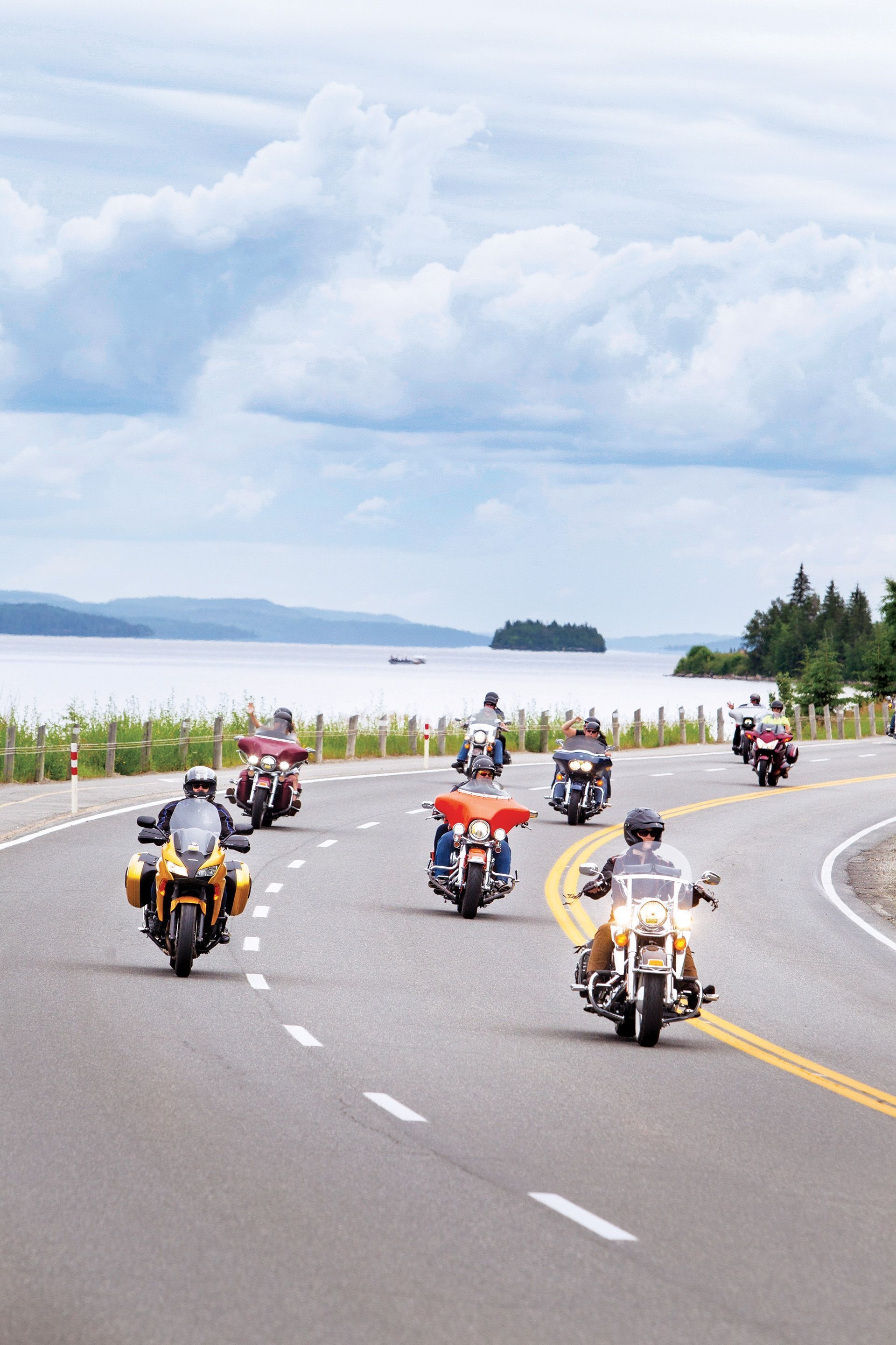 Sept conducteurs de moto empruntent une route sinueuse près d’un lac.
