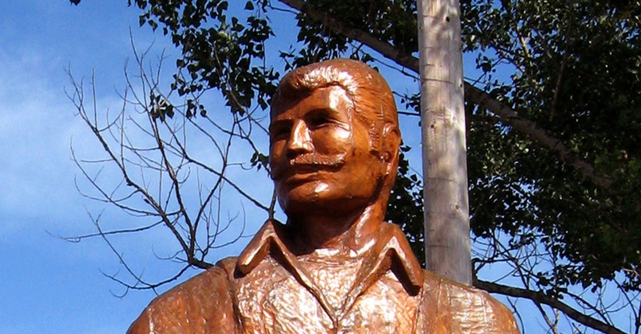 Gros plan sur le visage de la statue de bois de Jos Montferrant. Il porte une chemise de voyageur et une imposante moustache. 