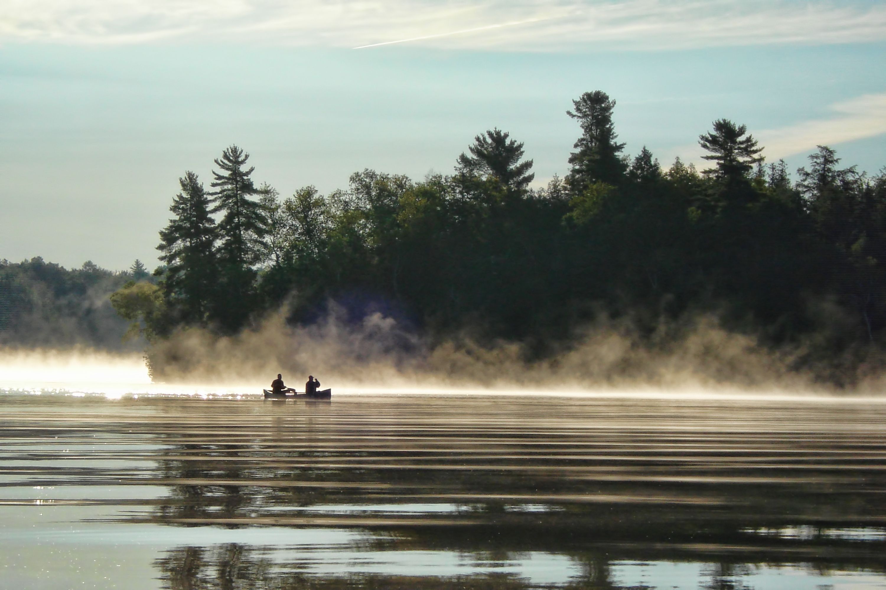 Deux personnes sont en canot sur un lac. La brume se lève. 