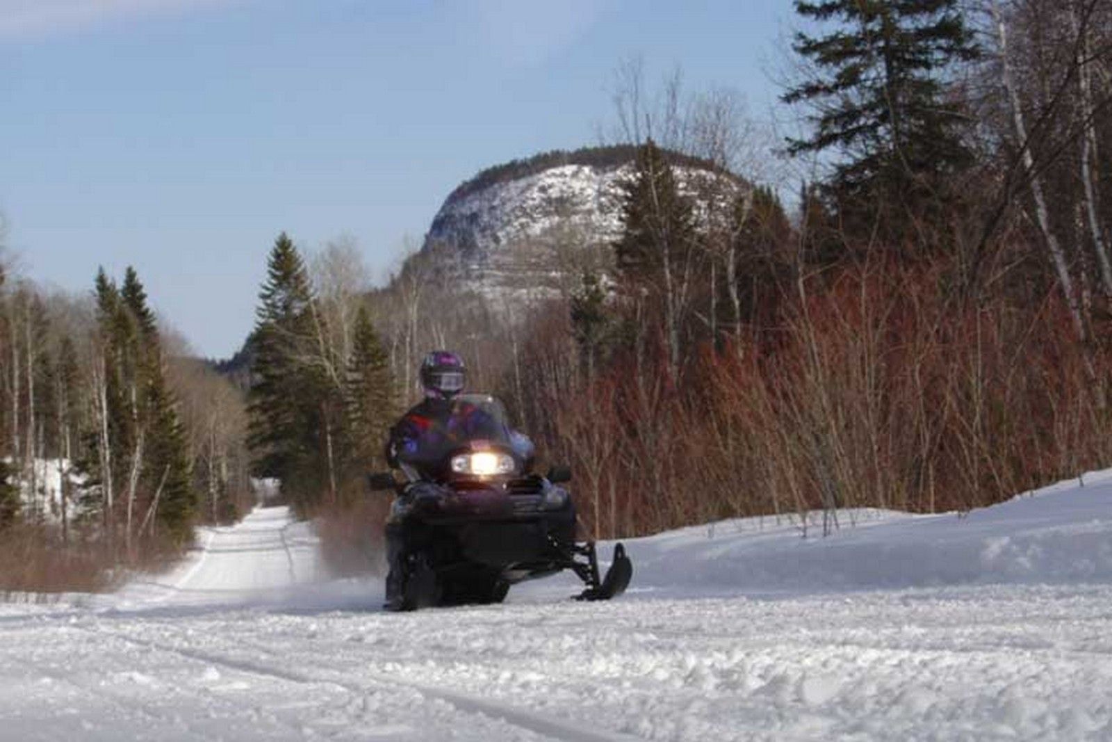 A snowmobiler rides along the trail in front of a large round mountain