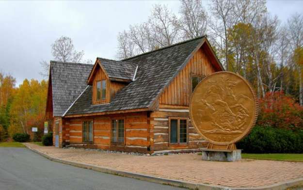 A large statue of a coin in front of a log cabin building