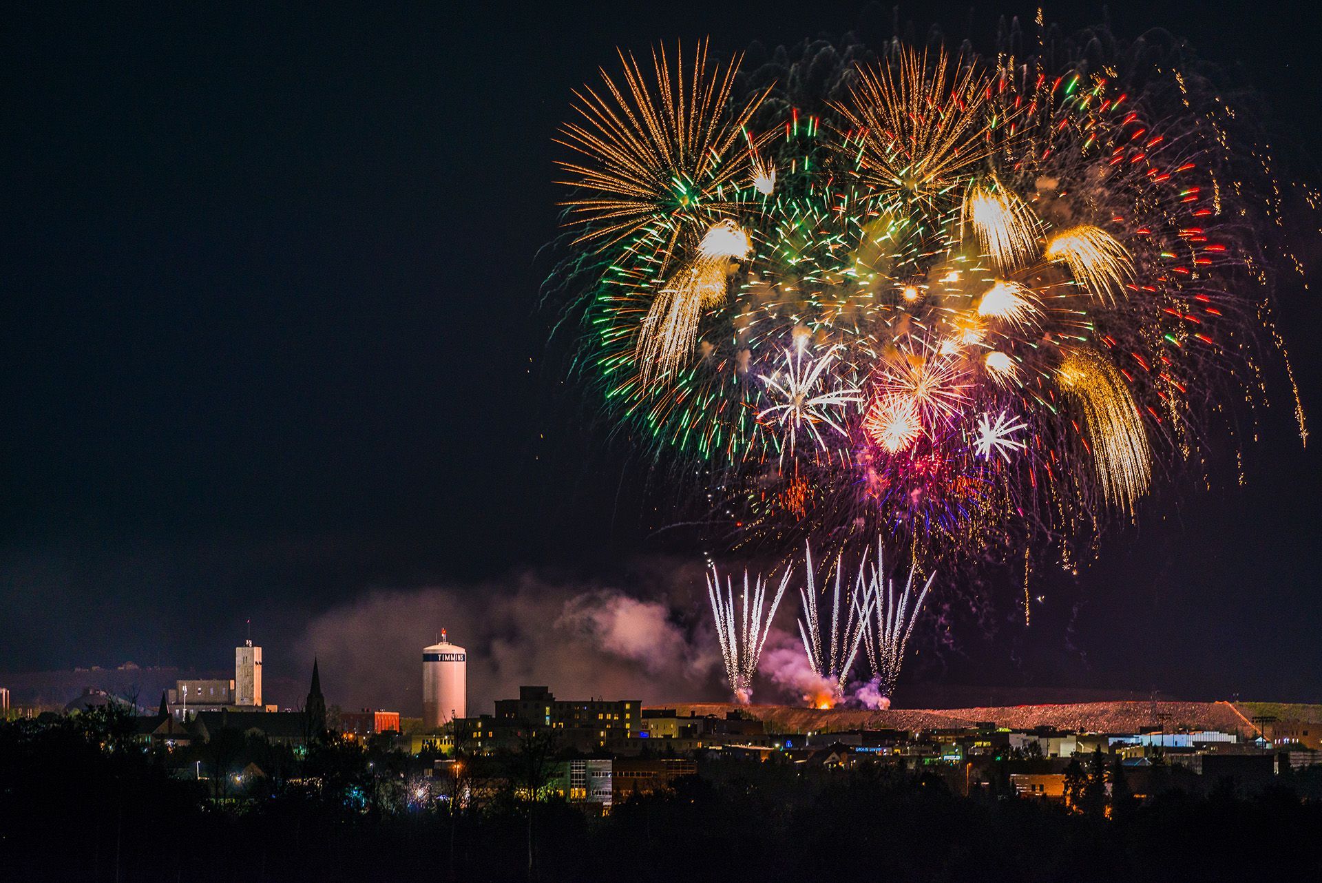 Un plan très large sur la ville de Timmins. On voit quelques bâtiments, mais surtout des feux d'artifice.