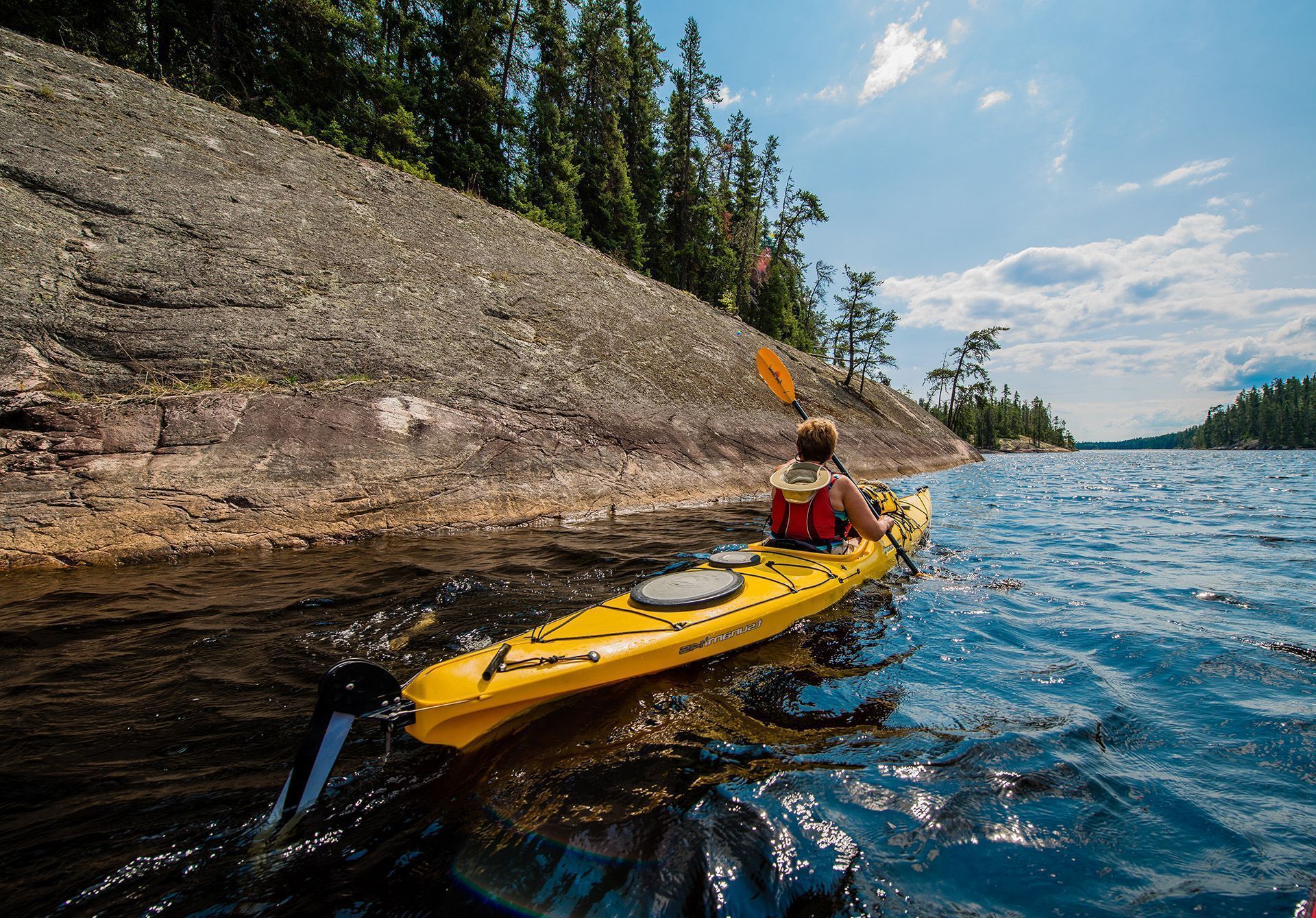 Une personne dans un kayak jaune vif pagaye à côté d’une paroi rocheuse au lac Kaneki, près de Timmins, en Ontario.