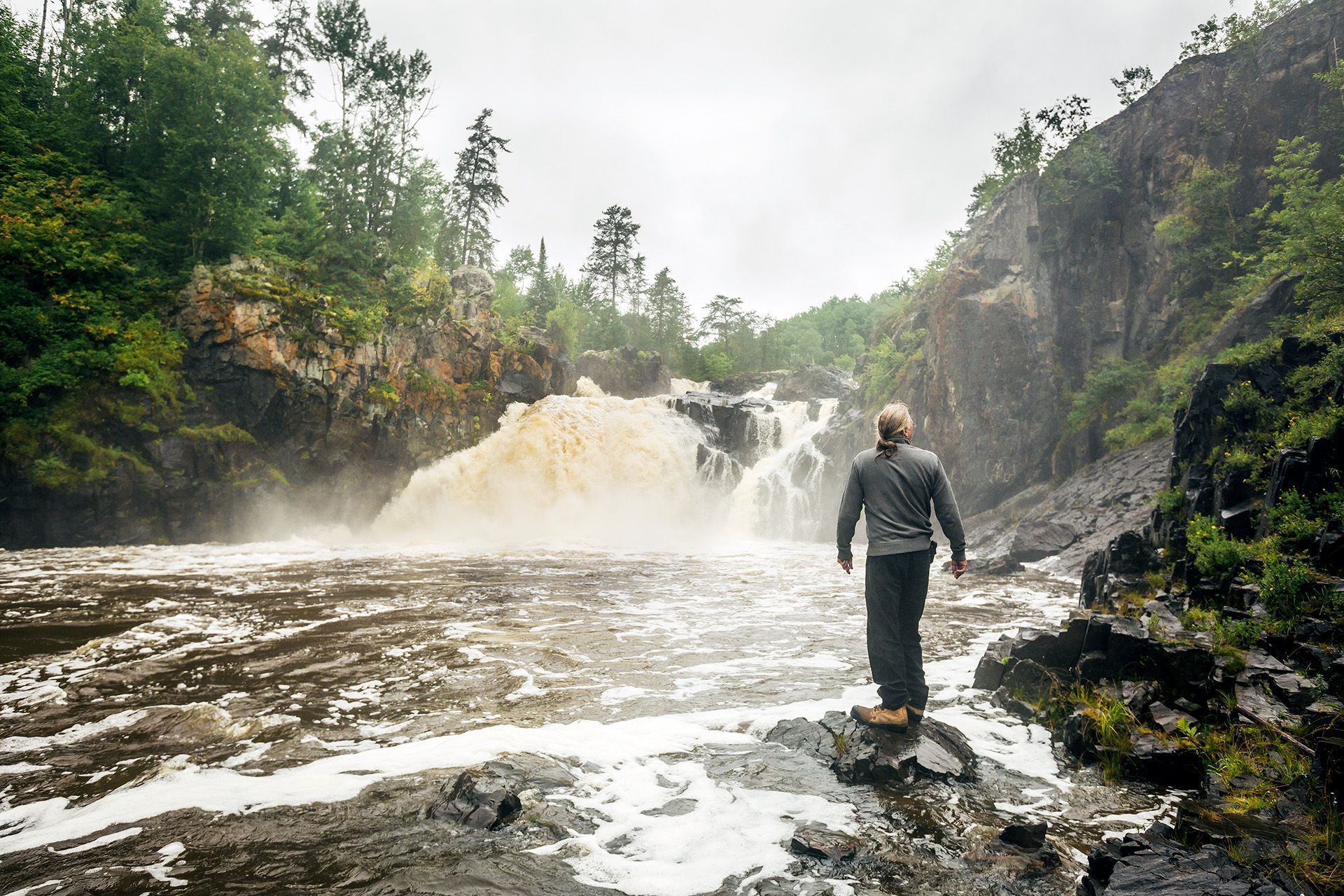 A person standing in front of a waterfall on Elk Lake trail at Kap-Kig-Iwan Provincial Park.