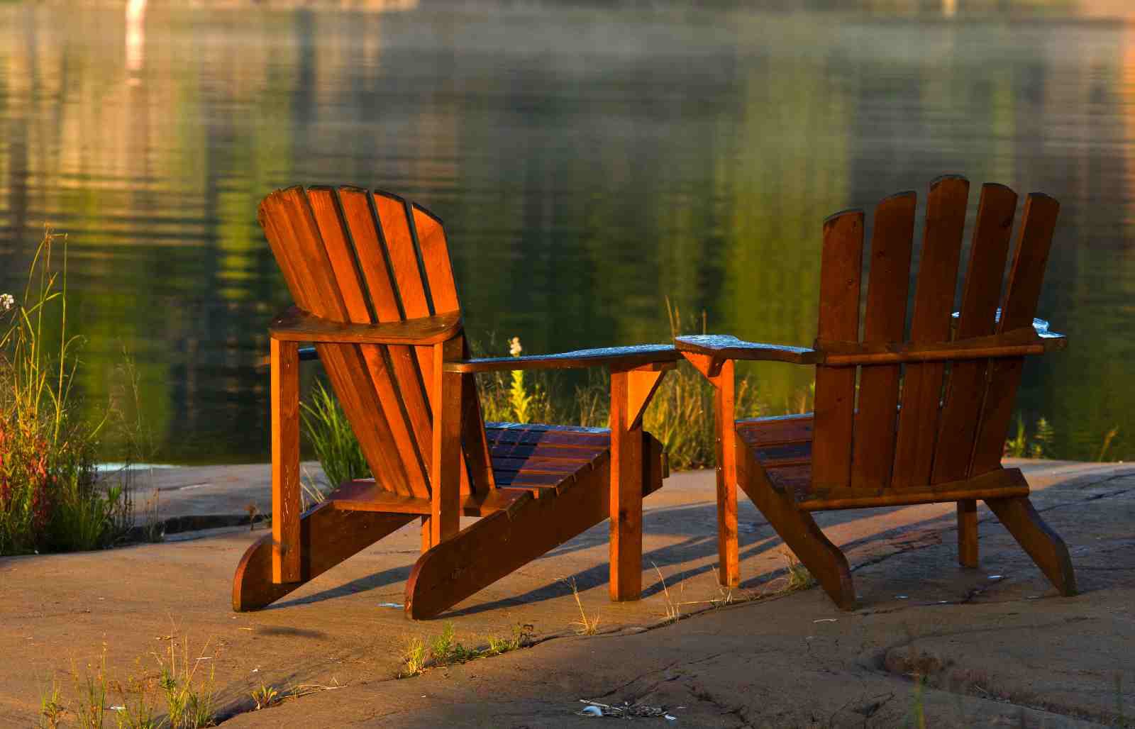 Two red muskoka chairs side by side in the sun.