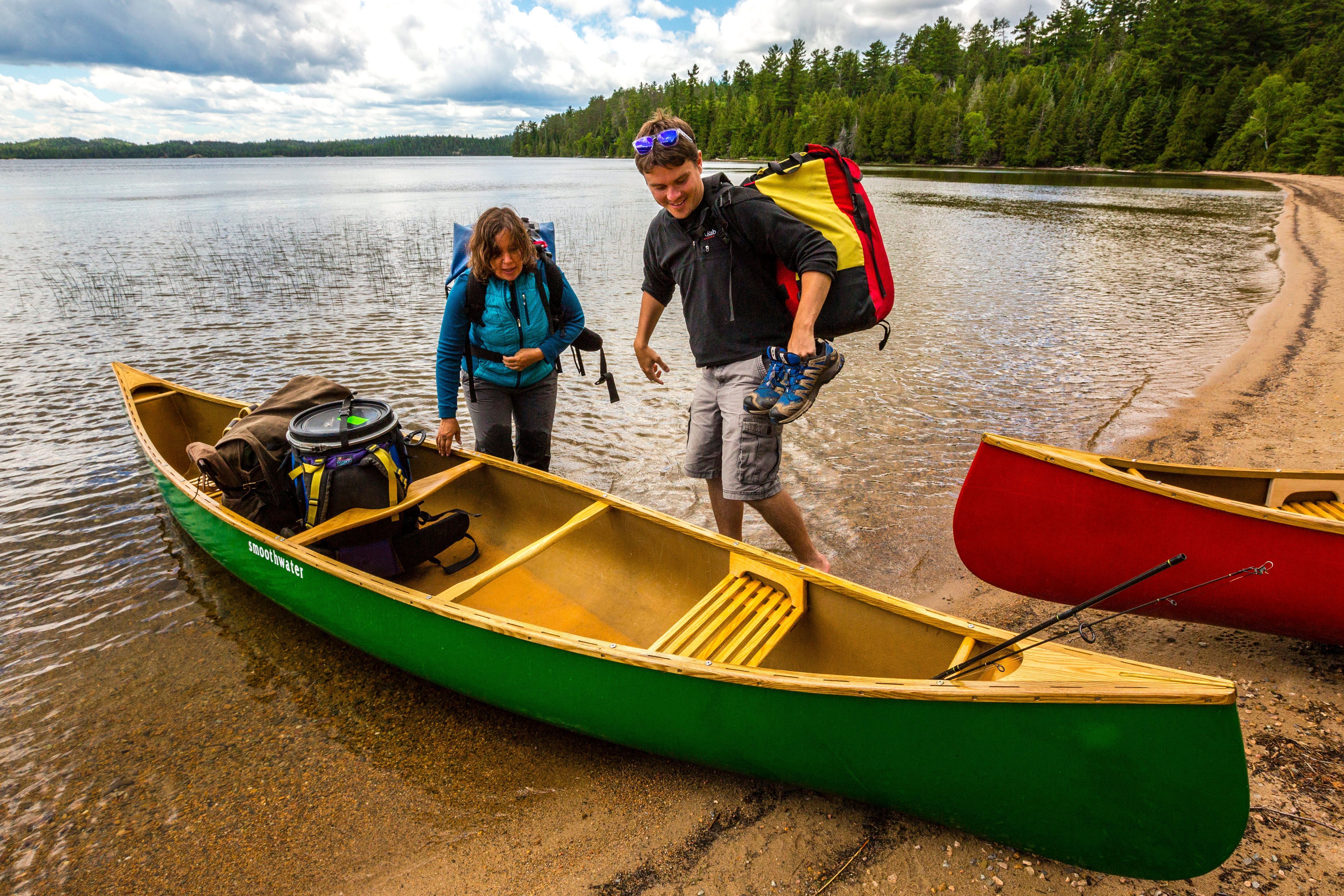 Two people with camping gear prepare to get into a green canoe