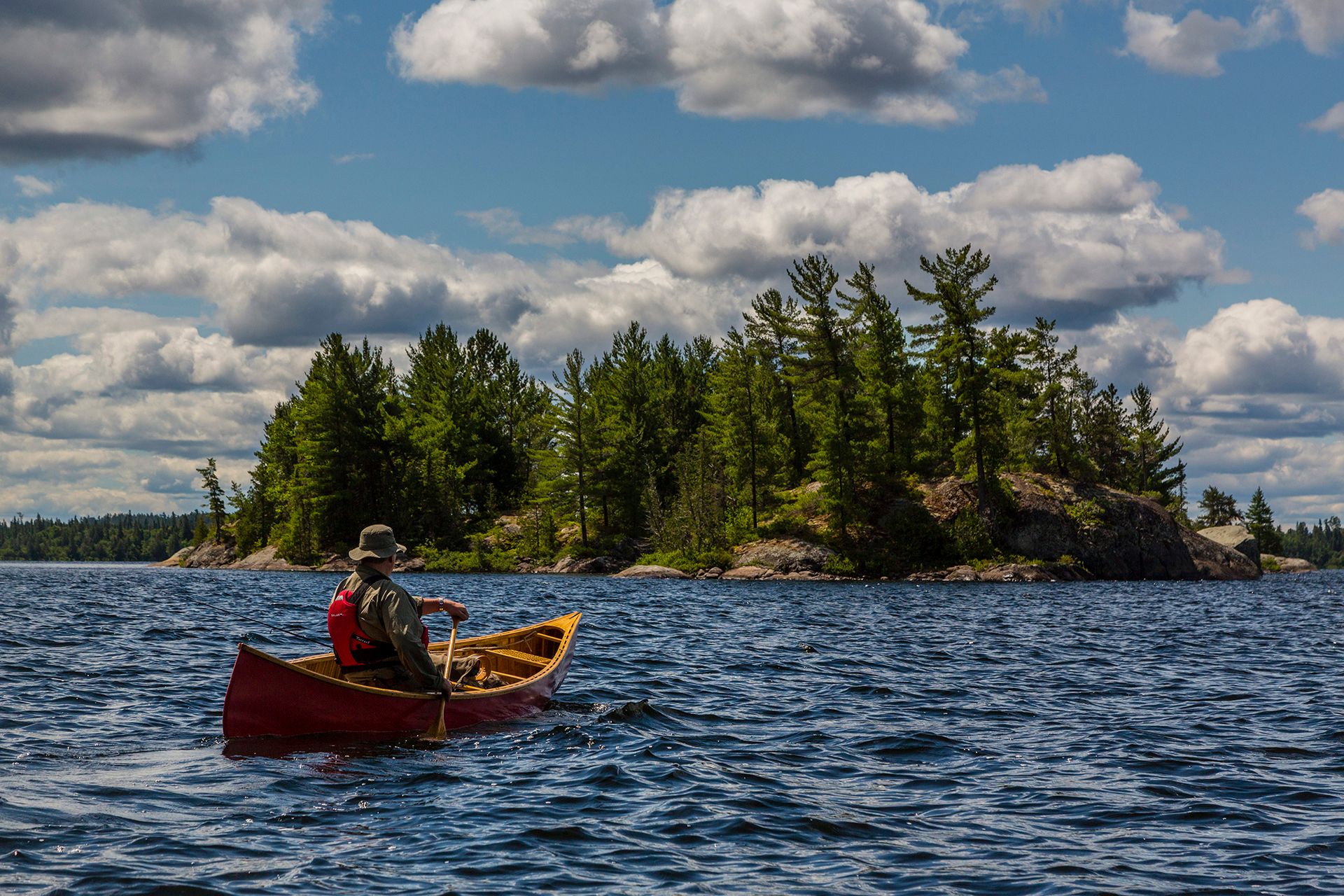 a man paddles a red canoe across a lake in front of a small island
