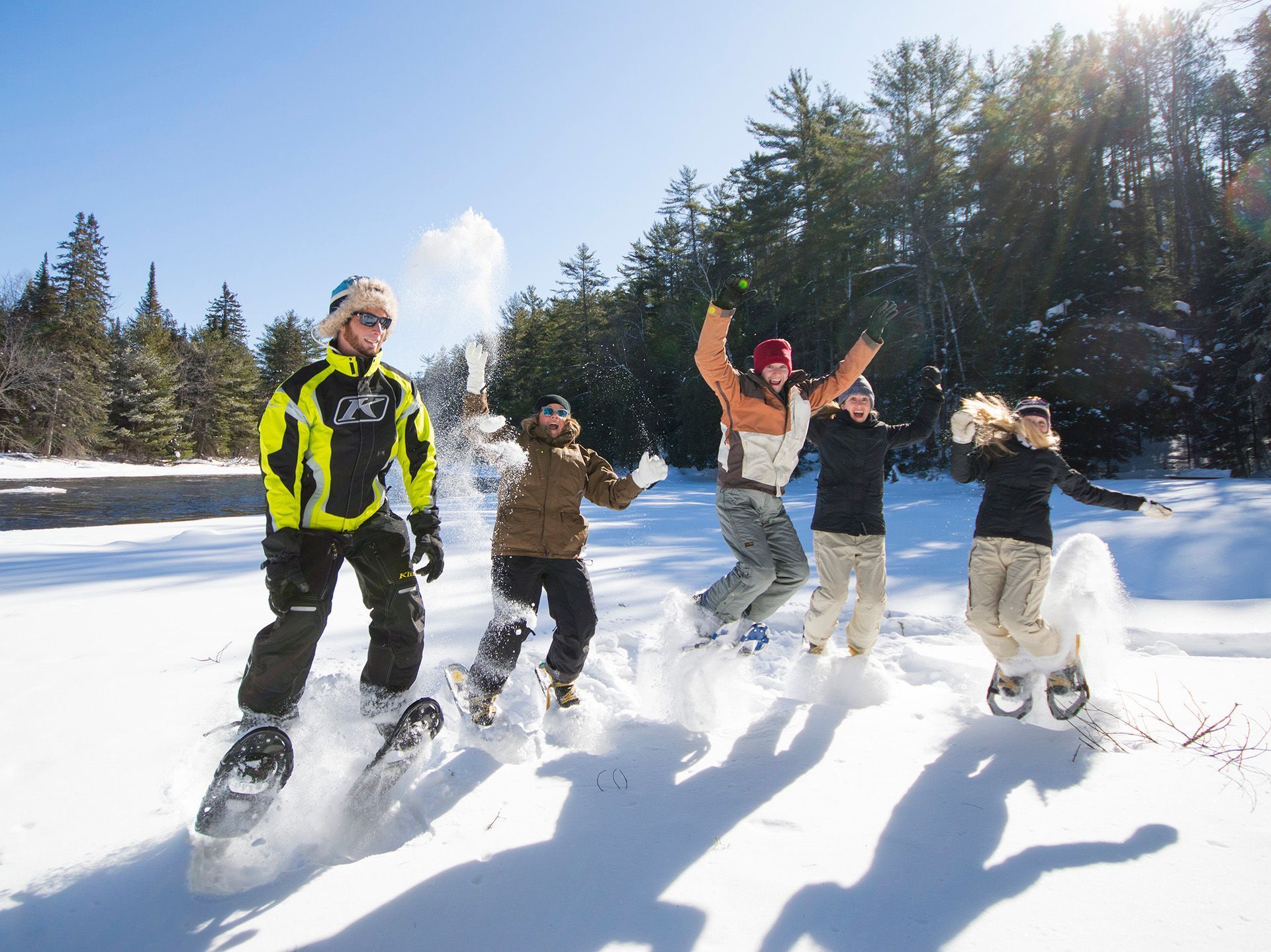 A group of people snowshoeing jump up excitedly and throw snow in the air