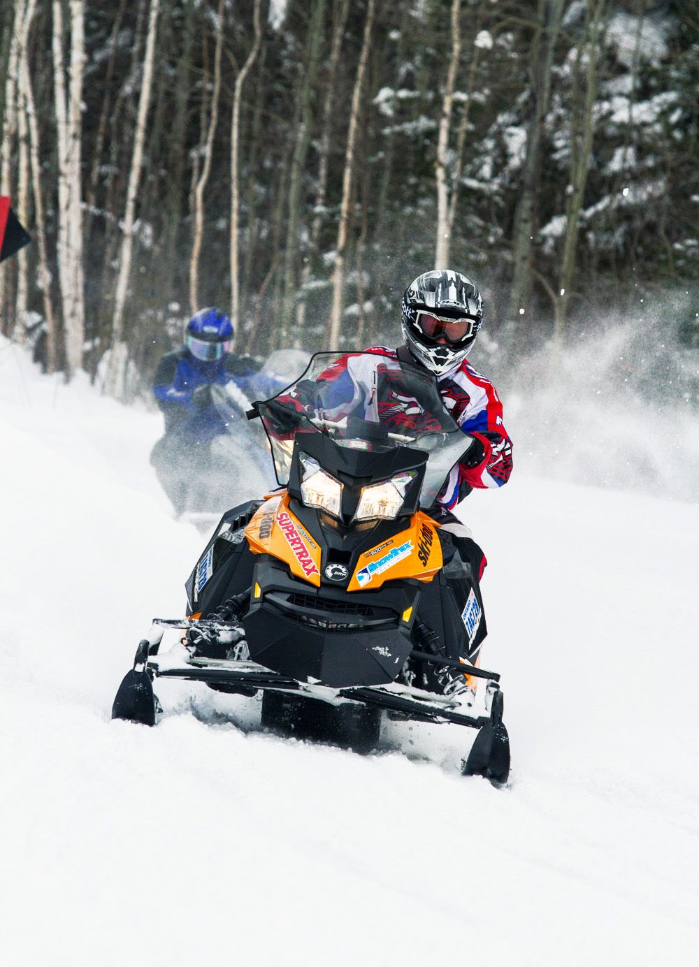 A person makes a tight turn on an orange snowmobile and kicks up some snow.